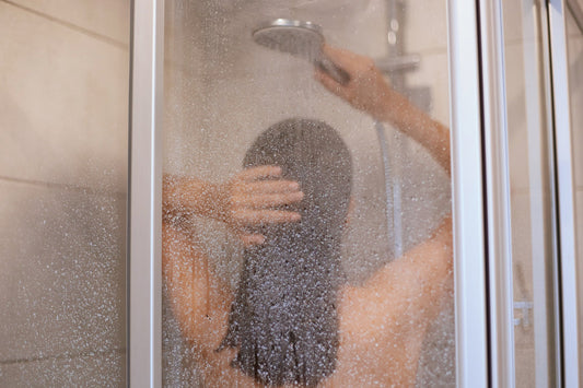 Hard water mineral deposits creating cloudy white spots on clear glass shower door surface