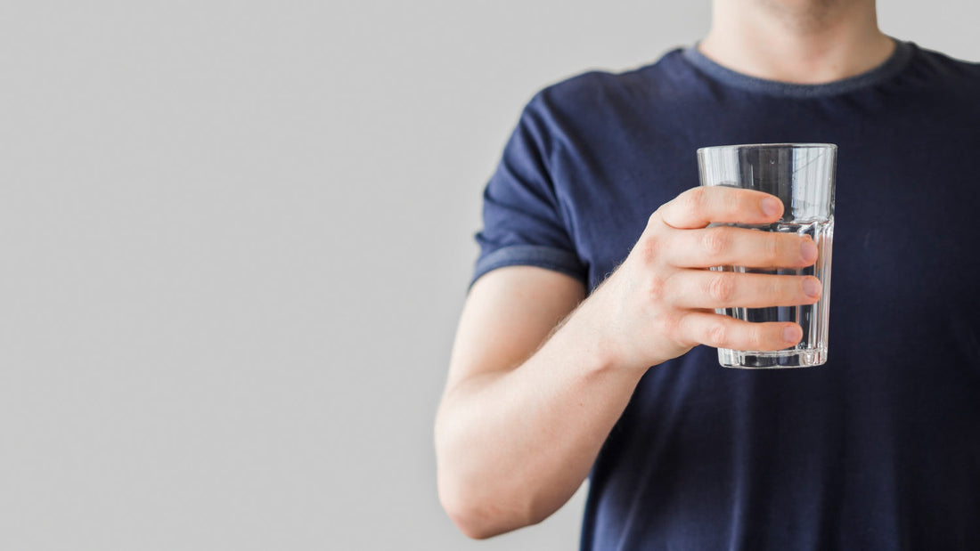 Person holding crystal clear glass of filtered water from coconut shell carbon block filter system