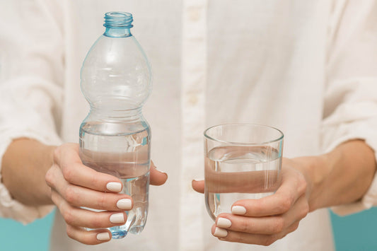 Bottled water vs filtered water comparison showing hands holding plastic bottle and glass of home filtered water