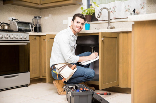 Homeowner installing under sink water filter system in modern kitchen cabinet with tools and instructions