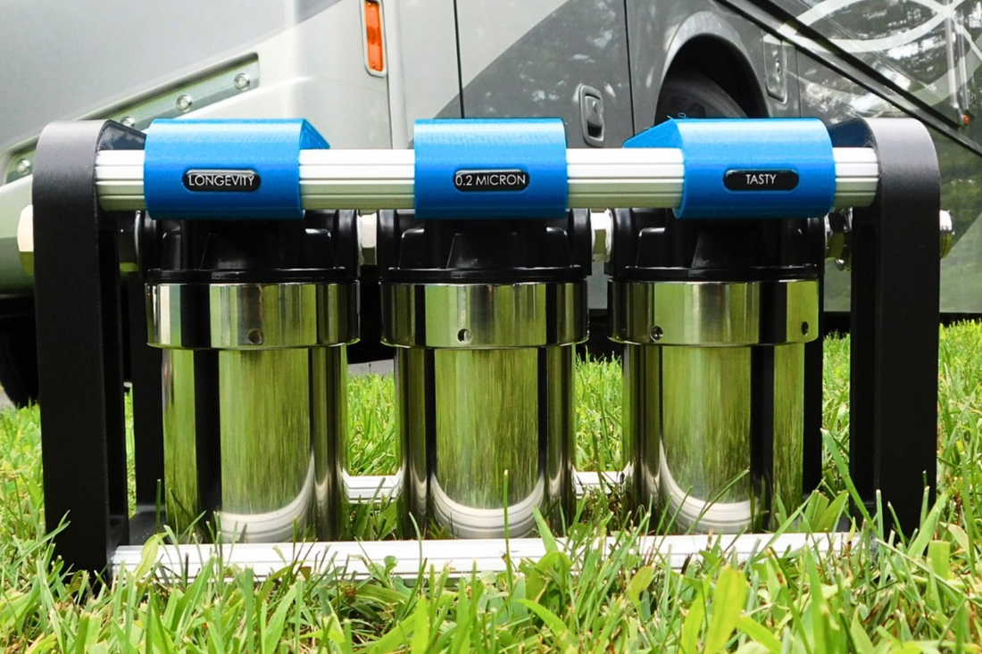 Three-stage portable water filter system with longevity 0.2 micron tasty labels beside RV camper on grass