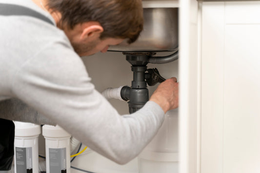 Homeowner installing under sink reverse osmosis system in modern kitchen cabinet setup with tubing visible